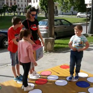 Deti hrajú nadrozmerné Človeče nehnevaj sa na chodníku pre budovou múzea.