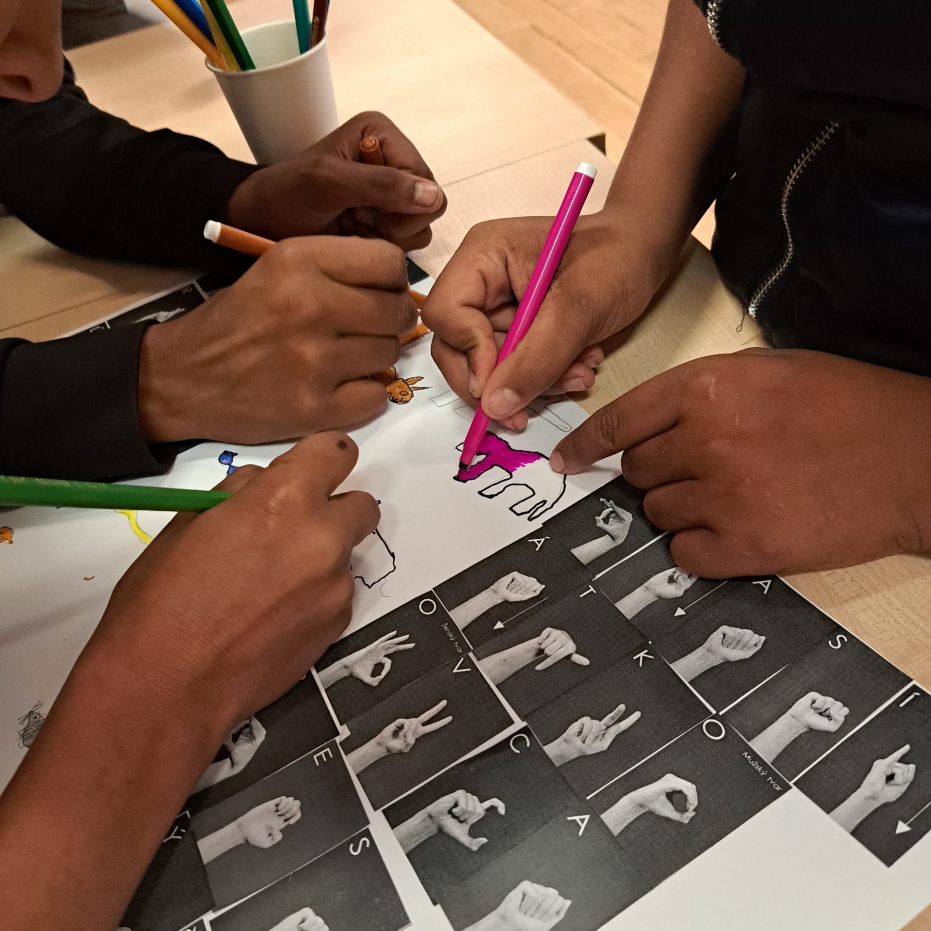 Deti vyfarbujúce obrázky zvierat. V popredí na papieri vytlačená prstová abeceda.