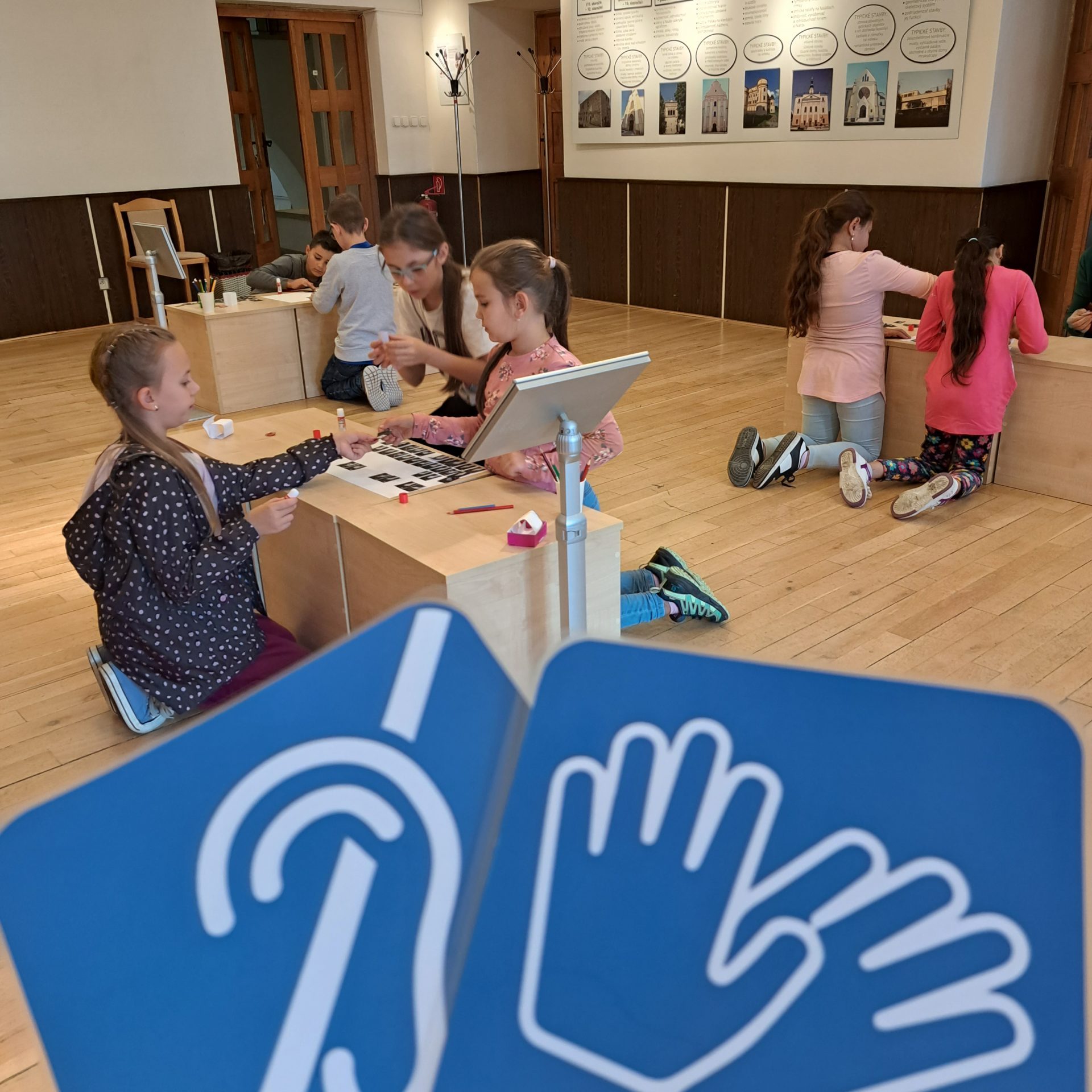 Deti v priestoroch Múzea špeciálneho školstva v Levoči počas edukatívneho programu o nepočujúcich. V popredí piktogramy.
