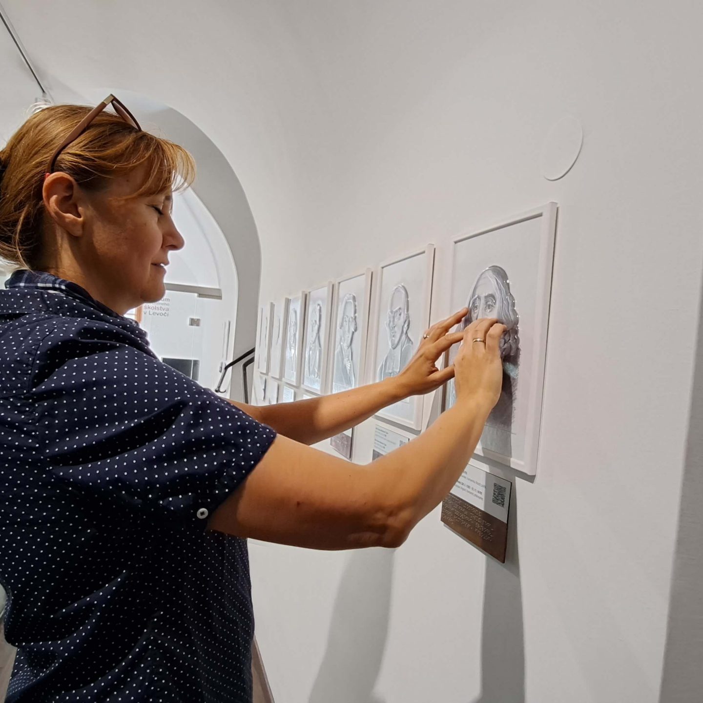 Návštevníčka Múzea špeciálneho školstva v Levoči hmatom prechádza portrét osoby.