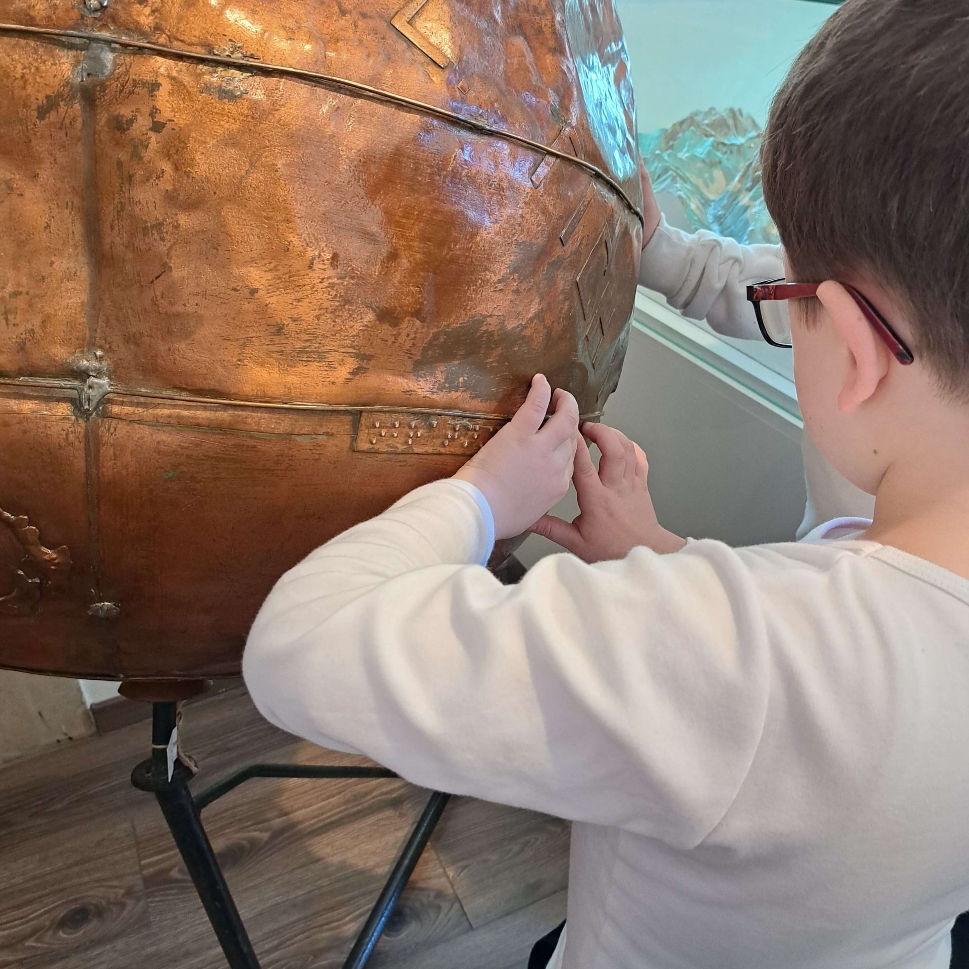 Návštevník sa dotýka medeného glóbusu v Múzeu špeciálneho školstva v Levoči.