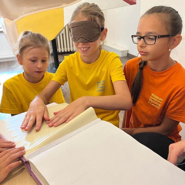 Návštevníci Múzea špeciálneho školstva v Levoči skúšajúci čítanie zo šlabikára pre nevidiacich.