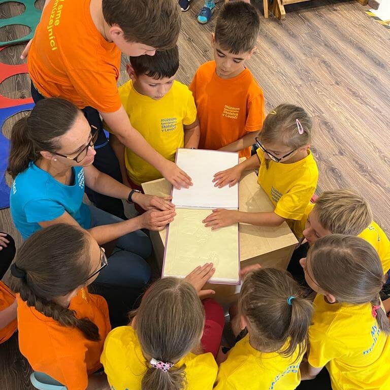 Návštevníci Múzea špeciálneho školstva v Levoči skúšajúci čítanie zo šlabikára pre nevidiacich.