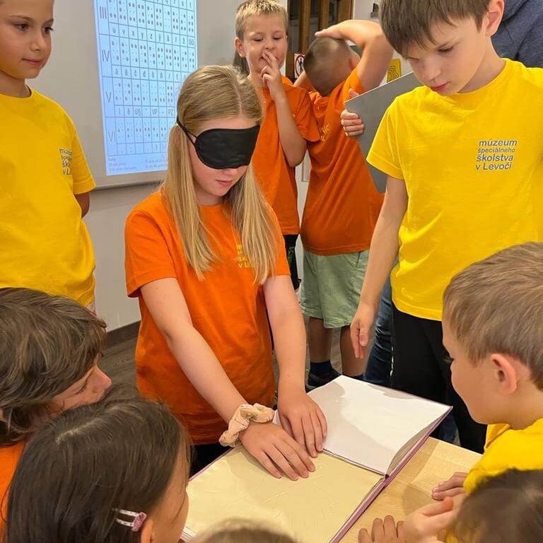 Šlabikár pre nevidiacich Návštevníci Múzea špeciálneho školstva v Levoči skúšajúci čítanie zo šlabikára pre nevidiacich.