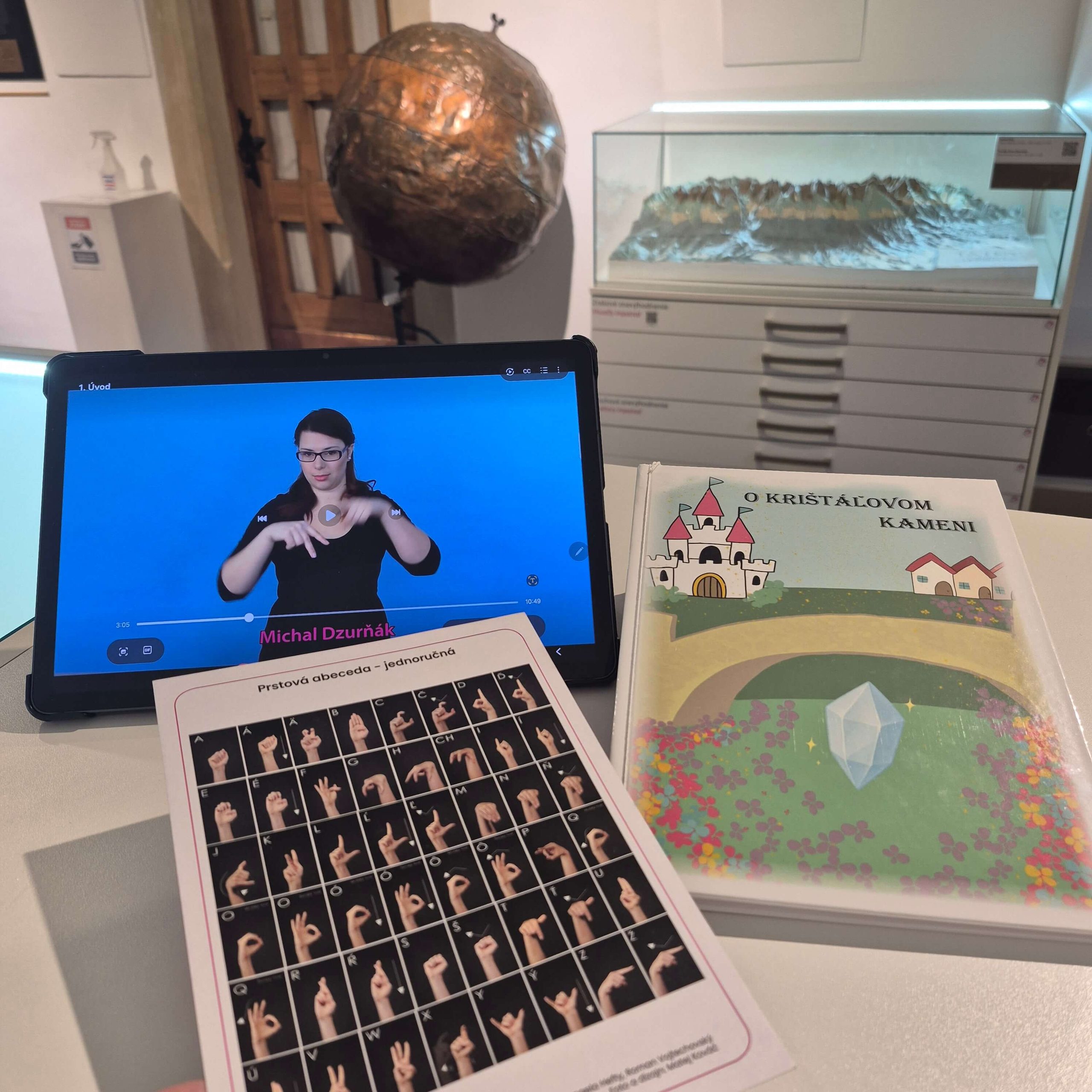 Prstová abeceda pre nepočujúcich, tablet s náhrávkou v posunkovom jazyku a kniha O krištáľovom kameni.